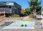 Crosswalk with sky blue background, sun, purple orange and blue buildings, and words that say PRUITT-IGOE, 1954-1976