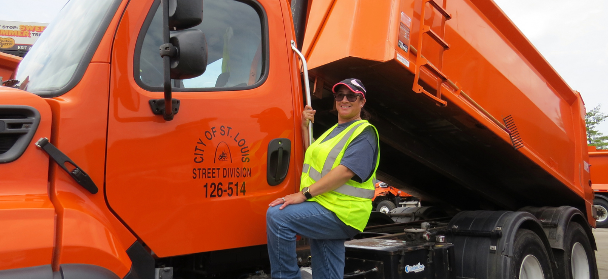 A photograph of a City employee standing next to a dump truck