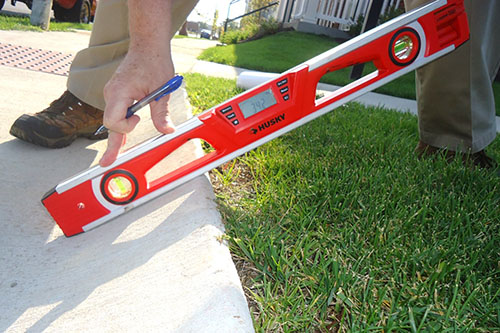 A person holding a level near a sidewalk